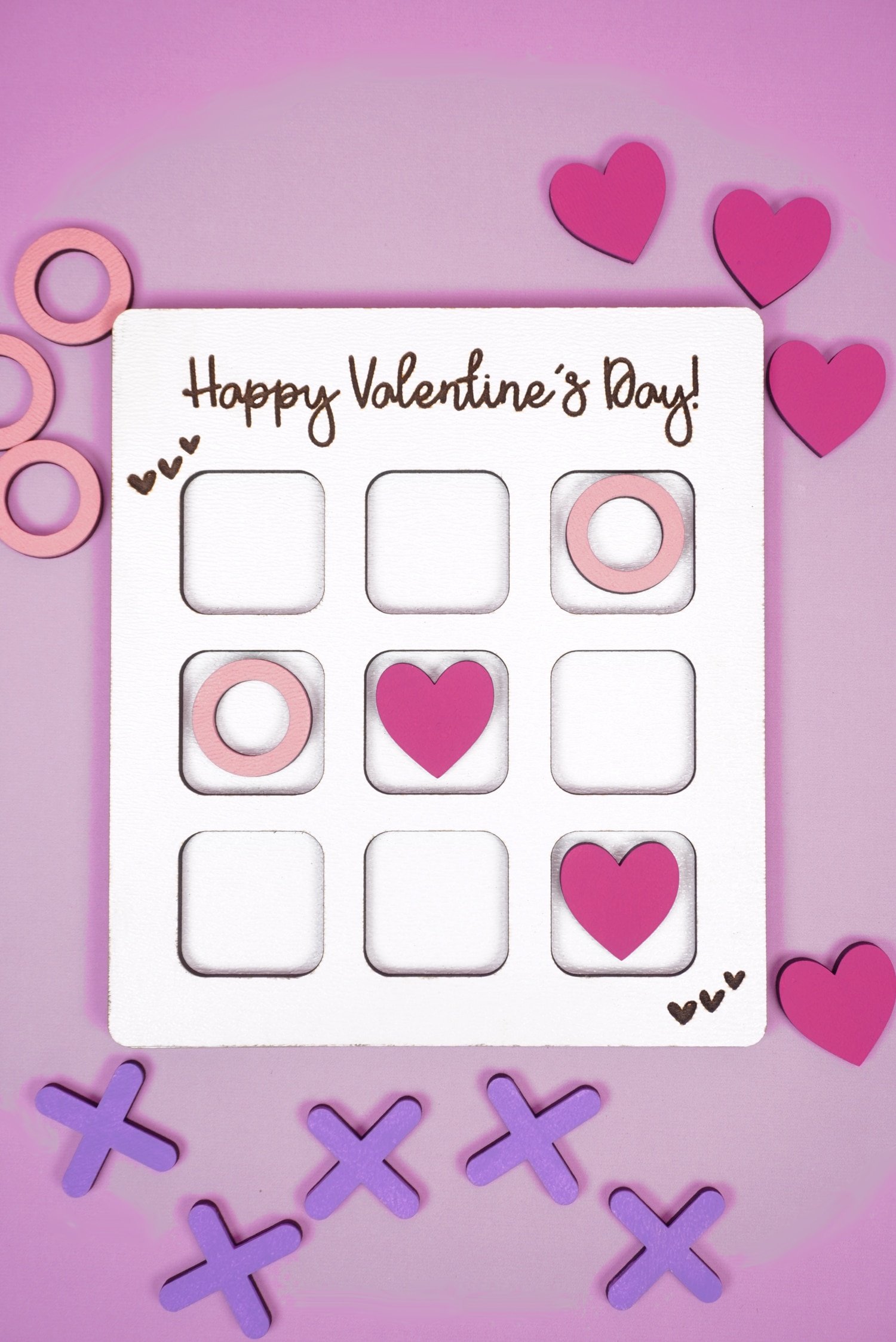 Valentine Tic Tac Toe game made with Glowforge laser SVG on a purple background with X's, O's, and pink hearts