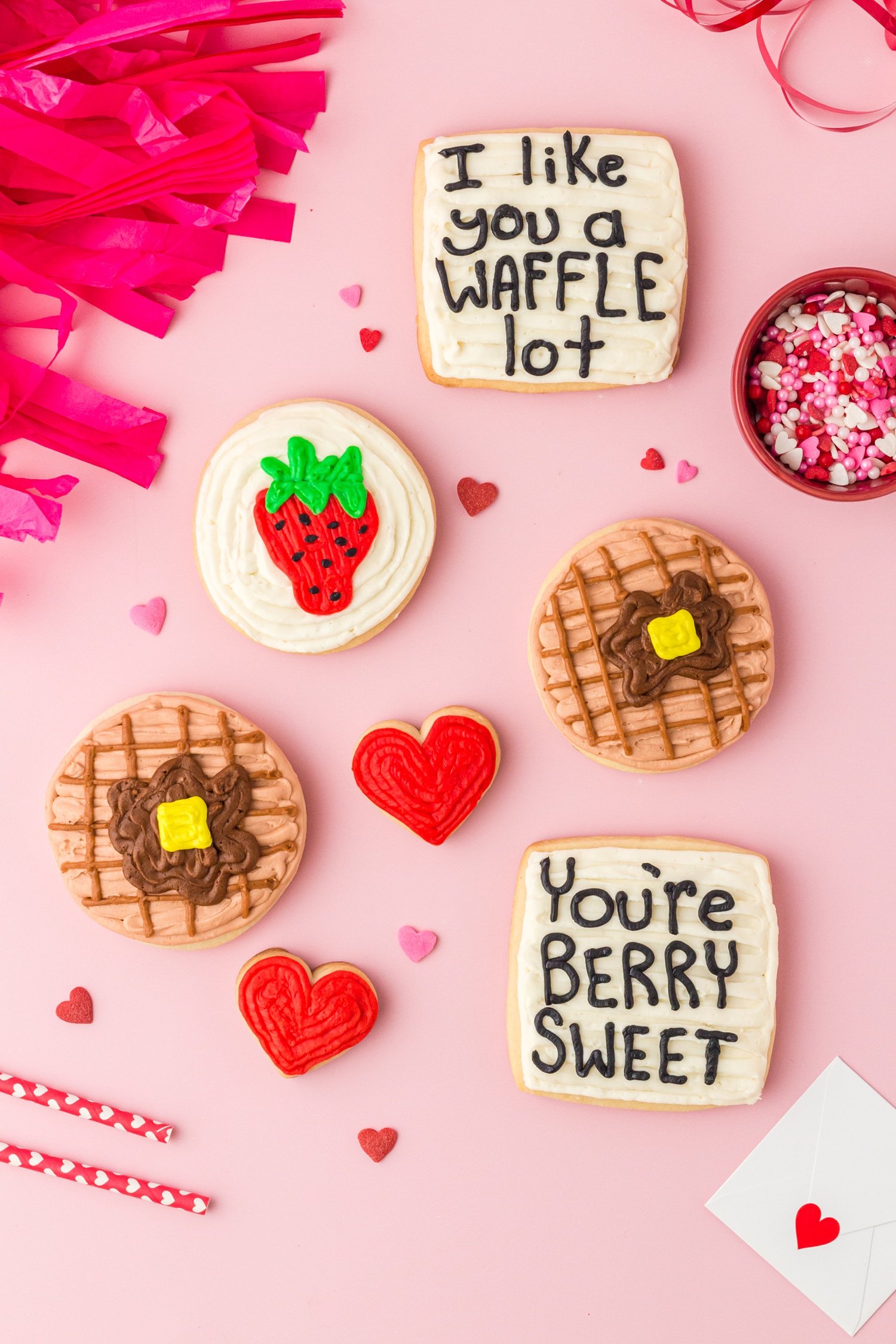 Waffle, strawberry, and heart sugar cookies with "I like you a waffle lot" and "You're berry sweet" cookies on pink background