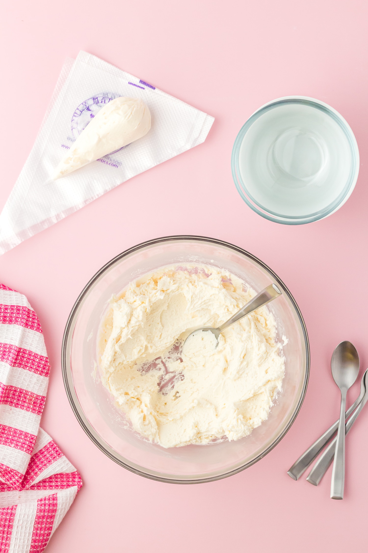 Mixing up sugar cookie icing with spoons and piping bag on pink background