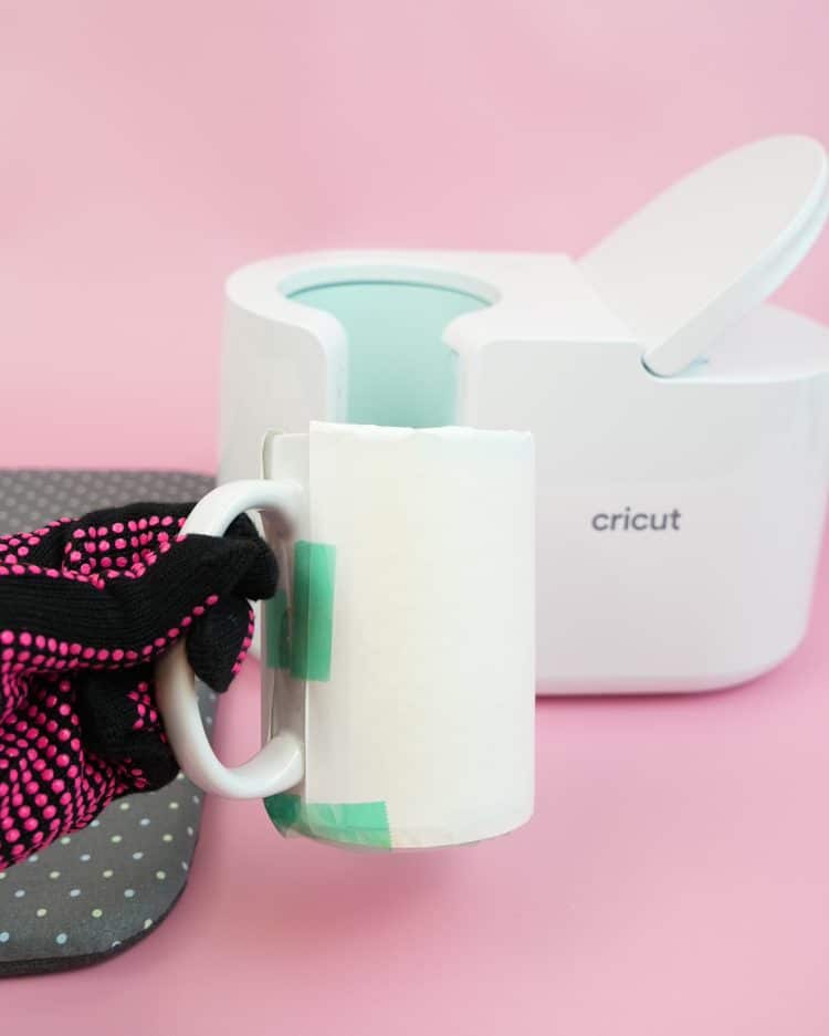 gloved hand removing mug from cricut mug press