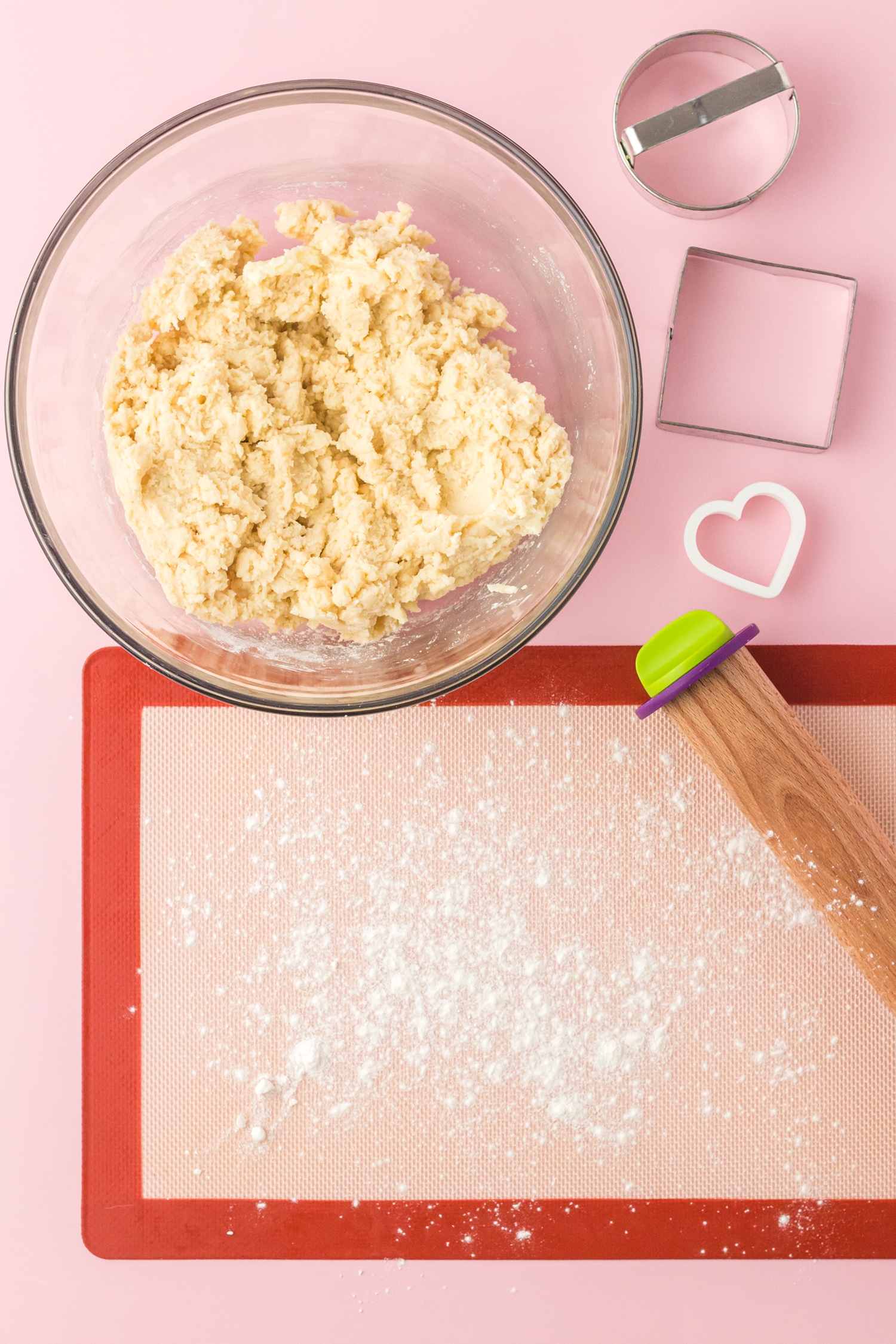 Sugar cookie dough in bowl and silicone mat with rolling pin on pink background