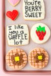 Waffle, strawberry, and heart sugar cookies with "I like you a waffle lot" and "You're berry sweet" cookies on baking sheet