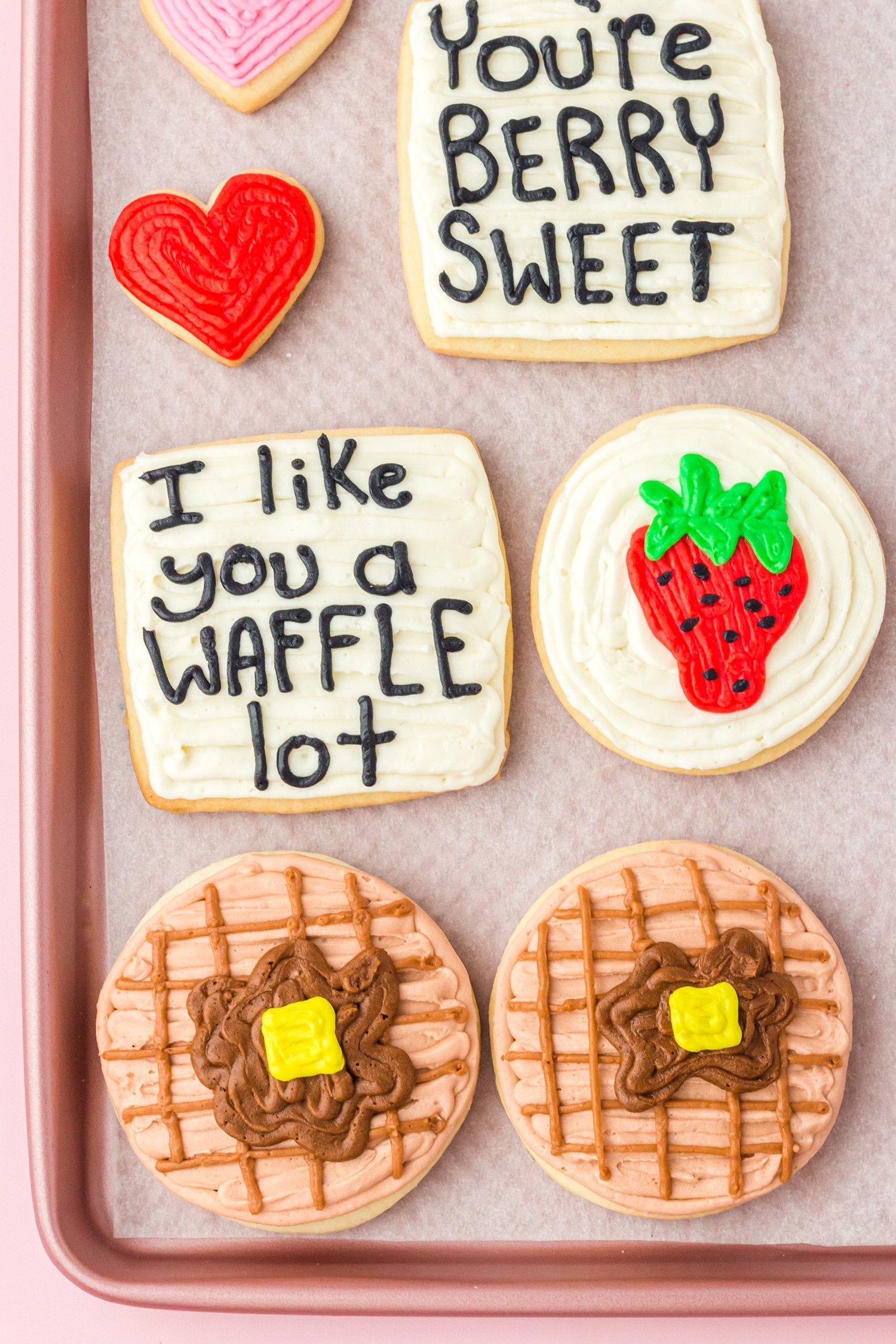 Waffle, strawberry, and heart sugar cookies with "I like you a waffle lot" and "You're berry sweet" cookies on baking sheet