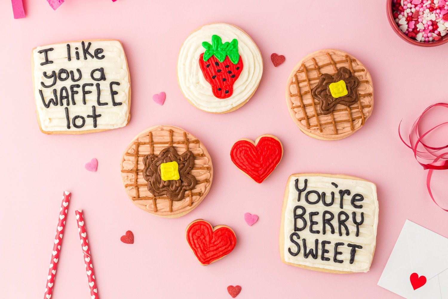 Waffle, strawberry, and heart sugar cookies with "I like you a waffle lot" and "You're berry sweet" cookies on pink background