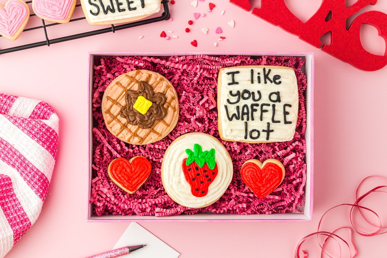 Assorted sugar cookies with waffle, strawberry, and heart motifs on pink valentine background