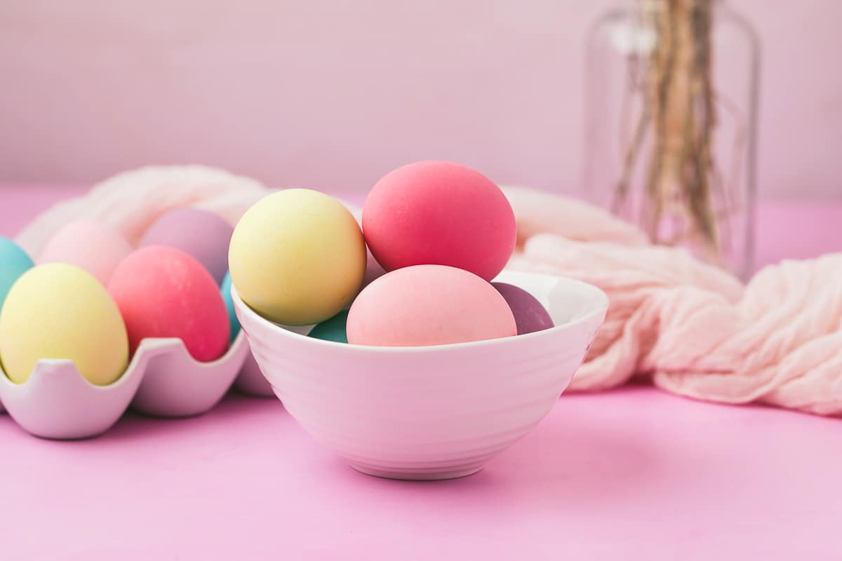 Bowl of brightly colored Easter eggs dyed with food coloring on a light purple background