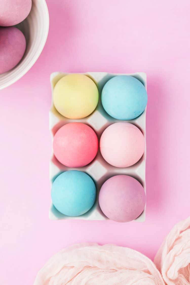 Colorful food-coloring-dyed Easter Eggs in a white tray on light purple background