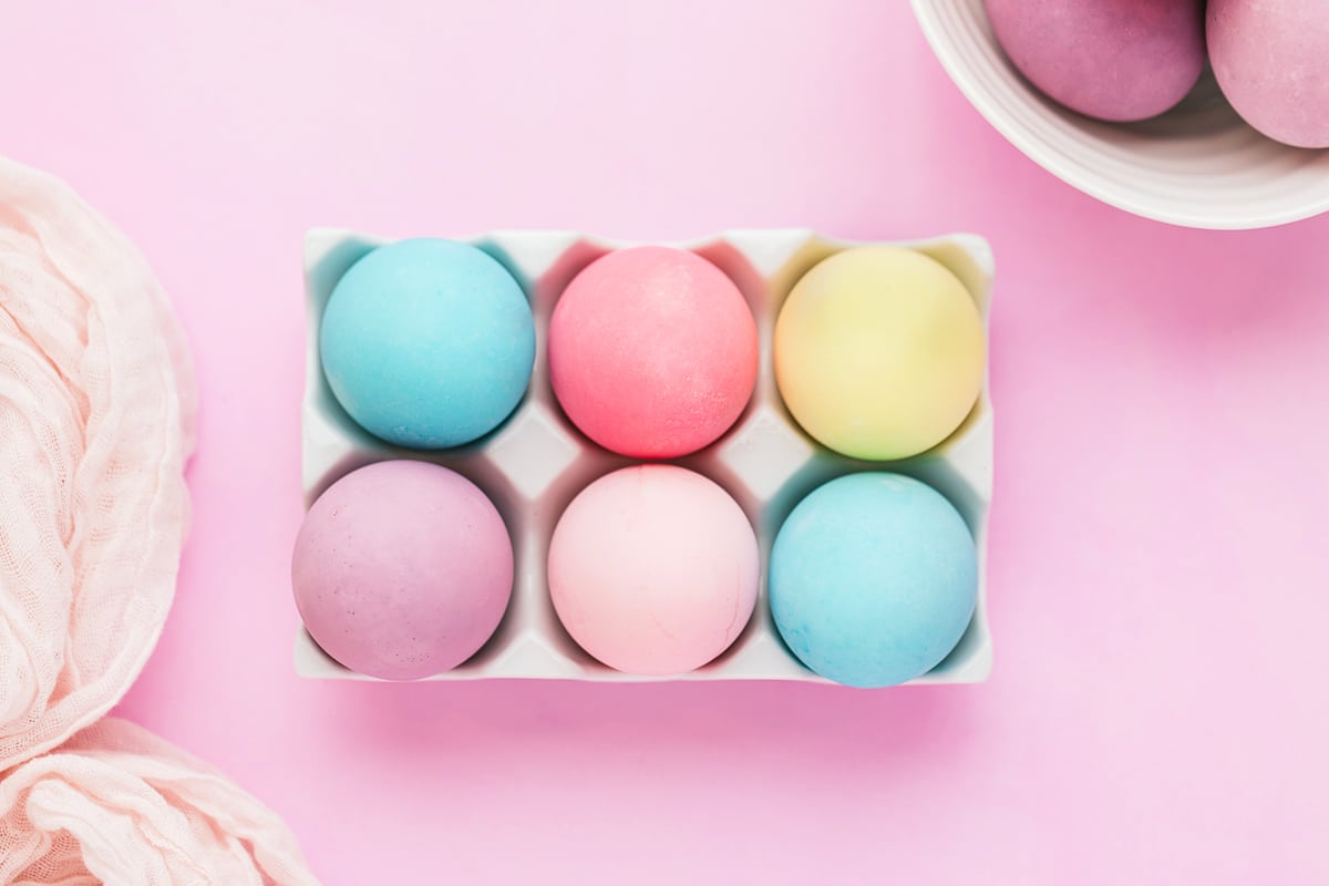 Colorful Easter eggs dyed with food coloring in white tray on purple background