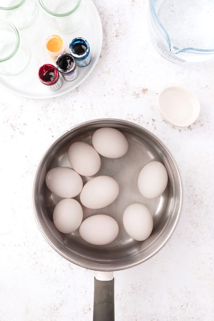 Hard boiled white eggs in a pot with food dye in the background