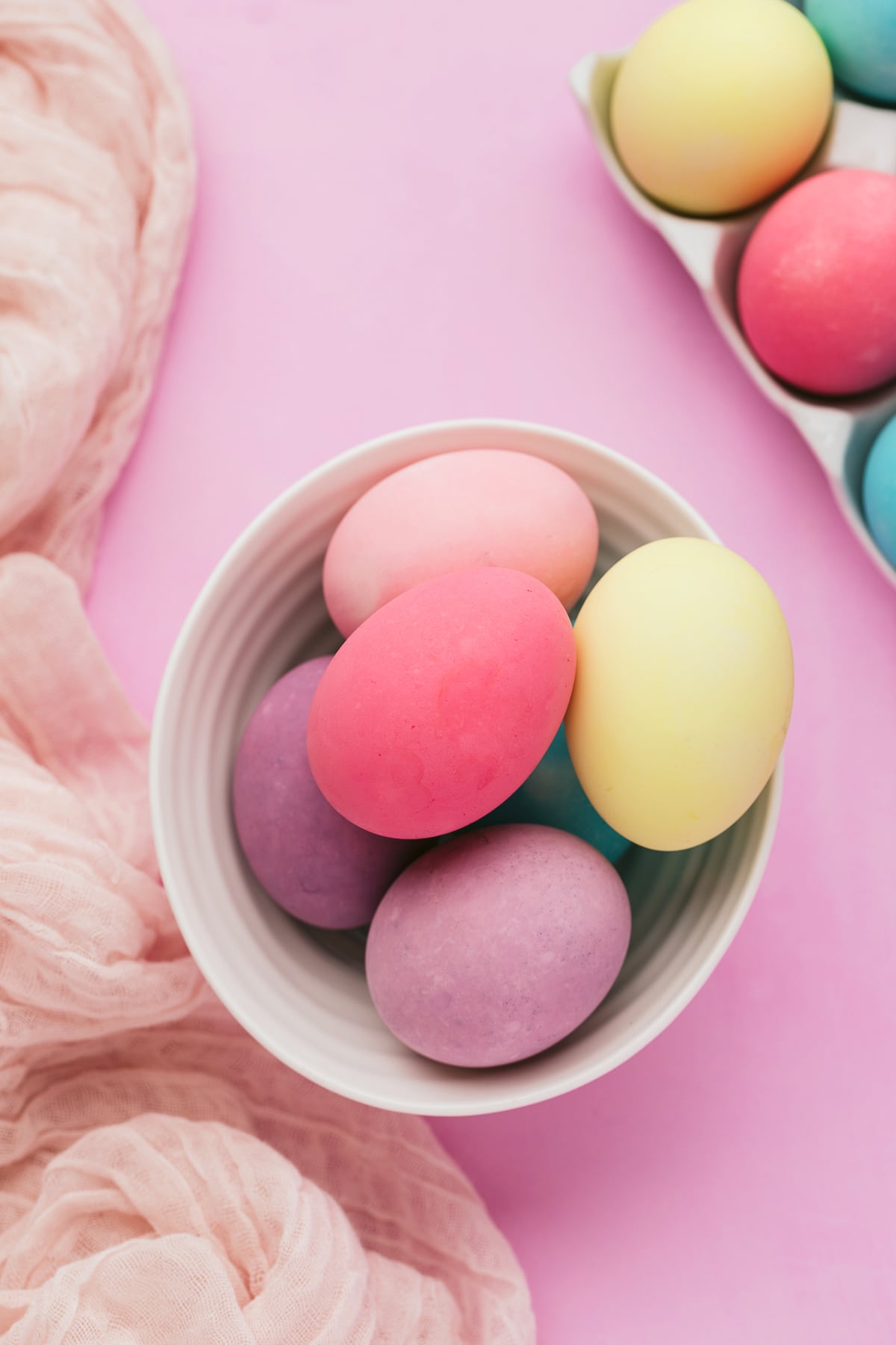 Colorful Easter eggs in a bowl on purple background with pink fabric