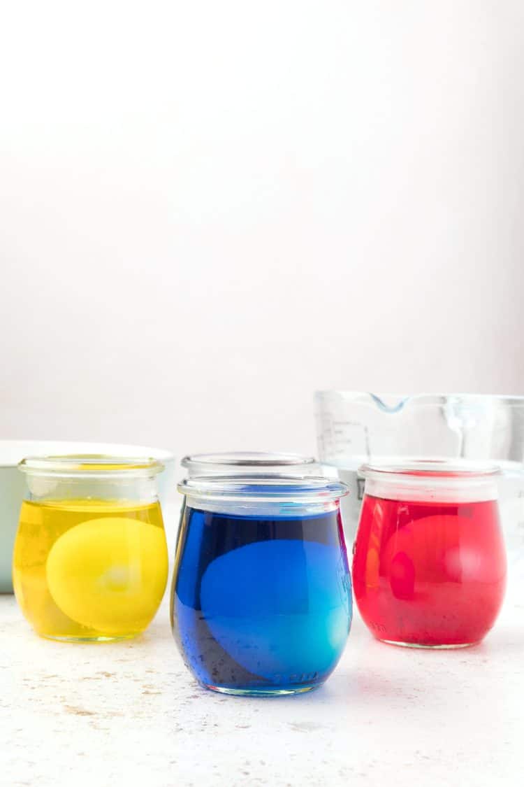 Three glass jars with yellow, blue, and red water dyeing Easter eggs