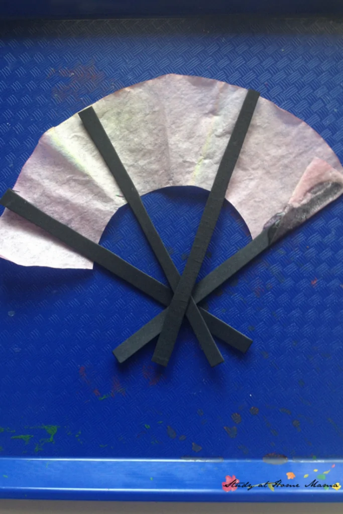 White coffee filter and black sticks assembled to look like a paper fan on blue background