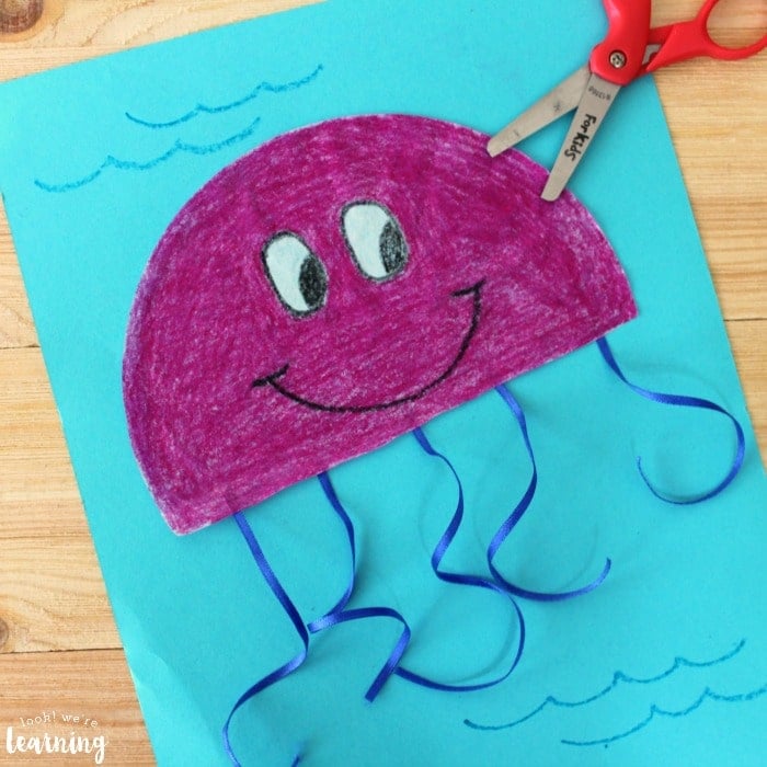 Purple coffee filter jellyfish with blue ribbon tentacles on light blue background.