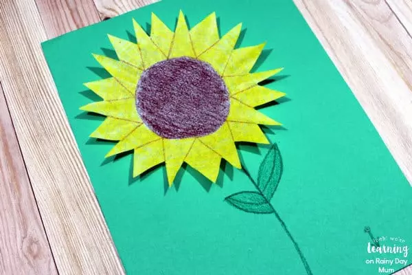 Coffee filter colored and cut to look like a sunflower on a green background.