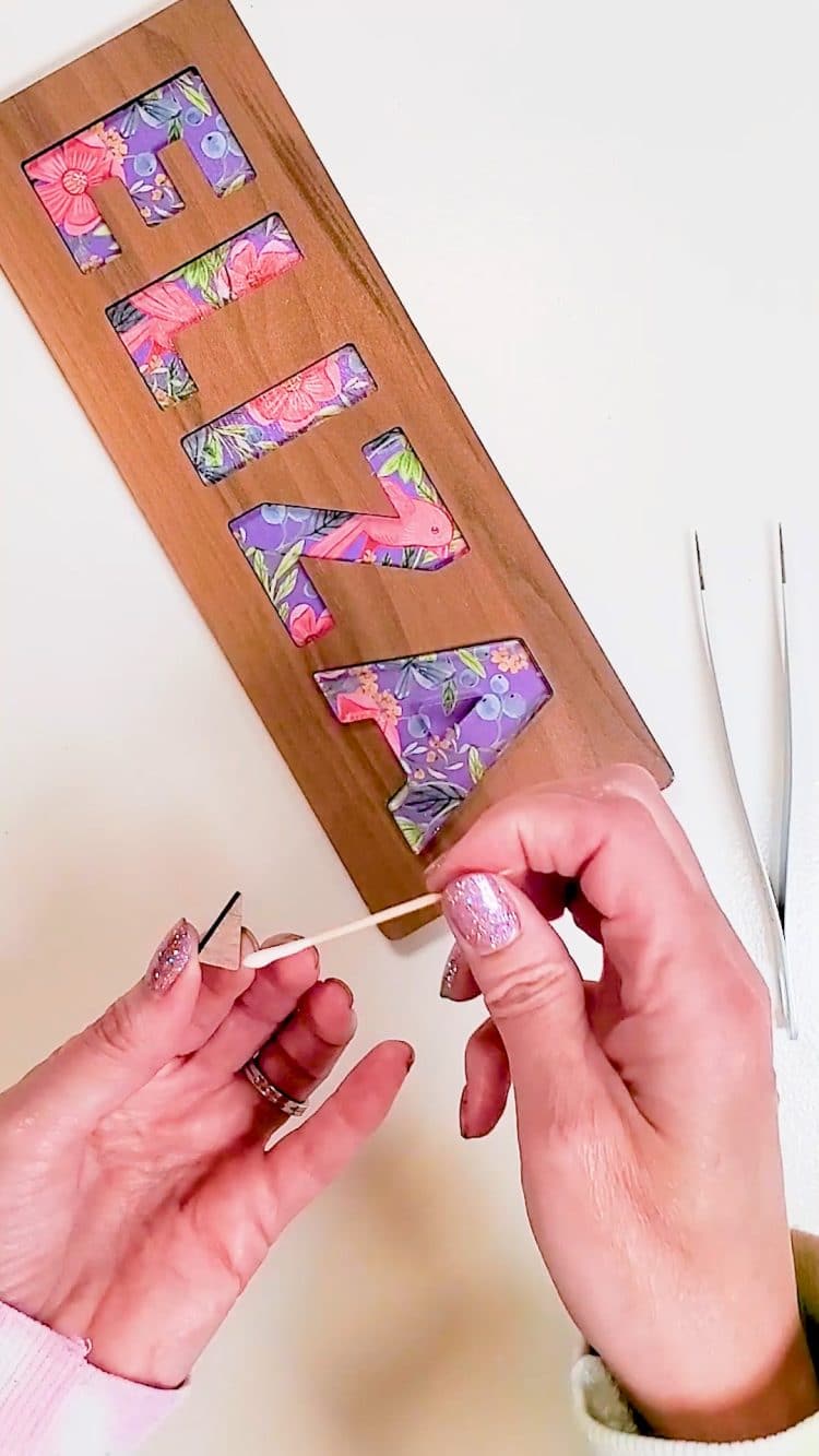 Hands adding glue to a small piece of wood for a custom name puzzle
