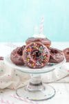 Chocolate donuts on cake stand with sprinkles and colorful straws on blue background