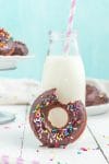 Close up of chocolate donut with sprinkles and missing bite with jar of milk in background