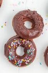 two chocolate donuts with chocolate icing and sprinkles on white background