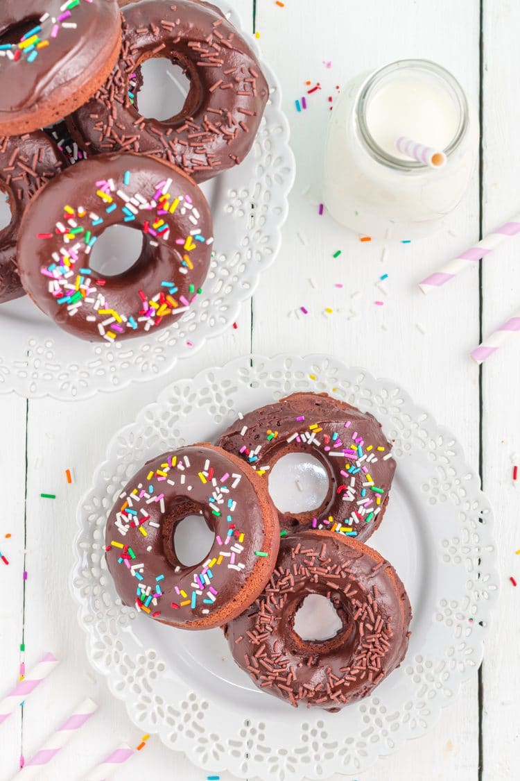 Overhead shot of sprinkled chocolate donuts on lacy white plate and cake stand