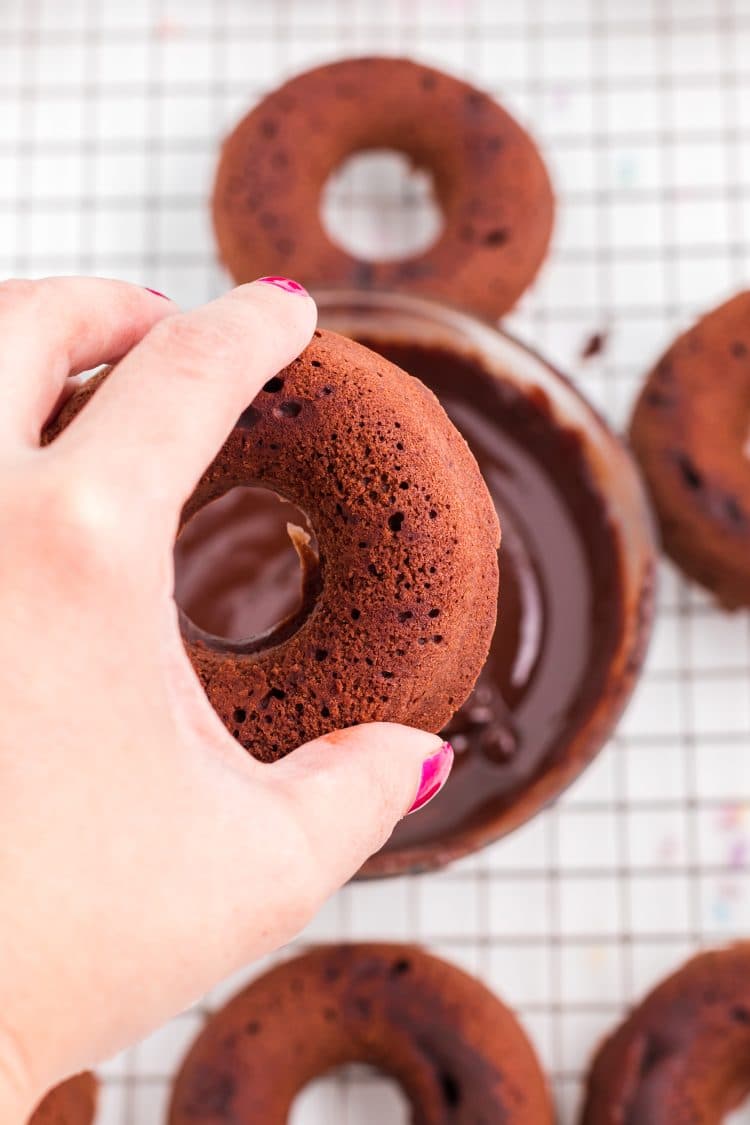 Hand dipping a chocolate donut in chocolate ganache icing