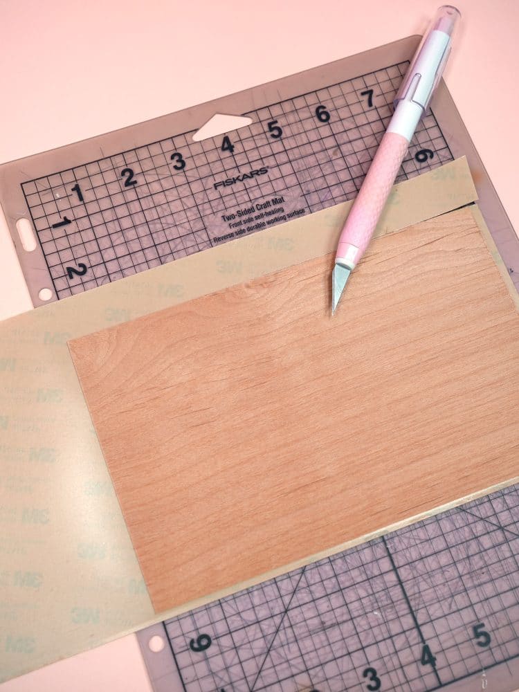 Using a craft knife to trim off excess 3M tape on peach background