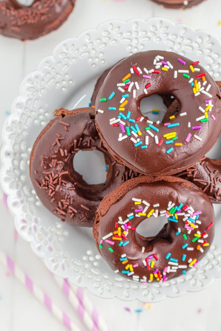 Chocolate sprinkled donuts on lacy white plate with sprinkles in background