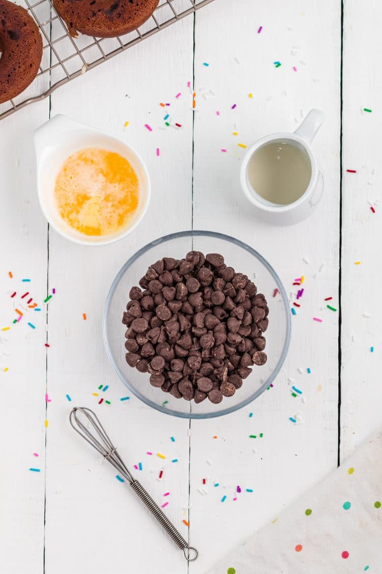 chocolate chips in a bowl surrounded by butter, cream, and a small whisk