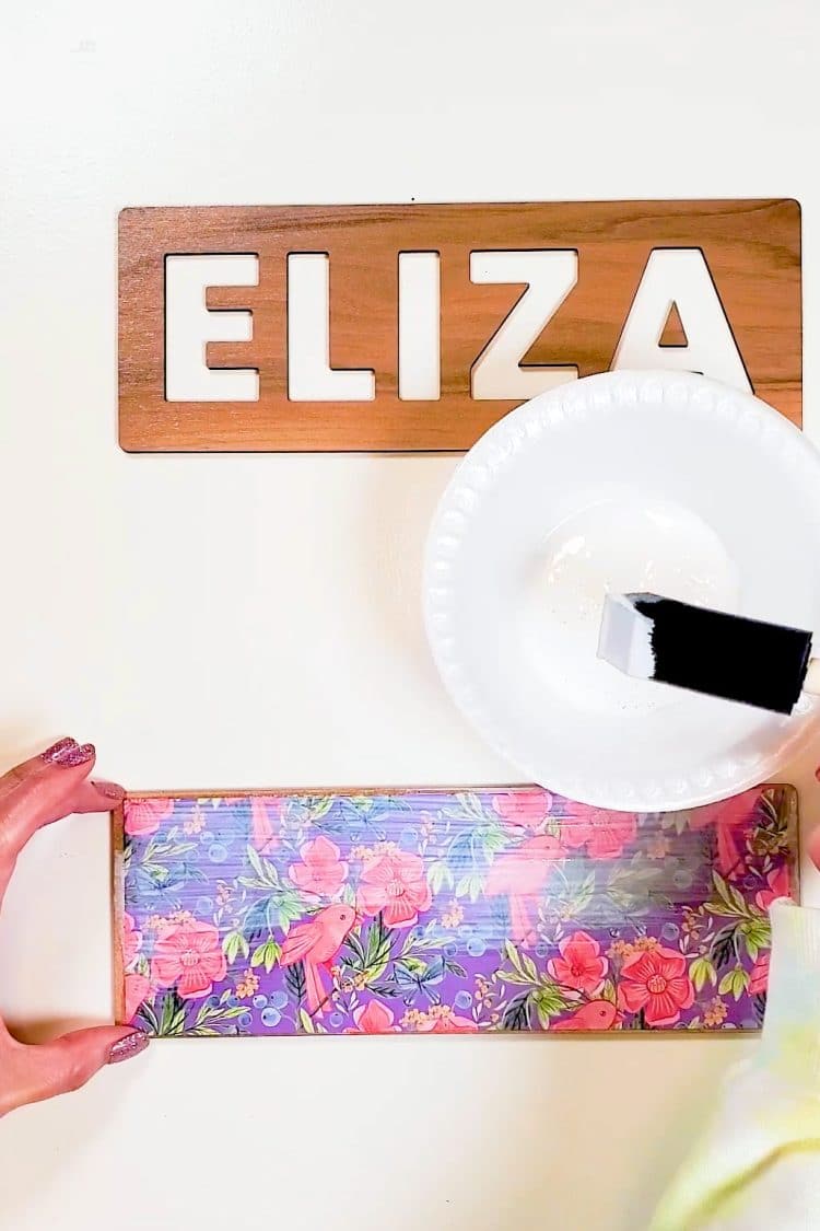 Hands applying Mod Podge to the top of patterned paper on a puzzle base