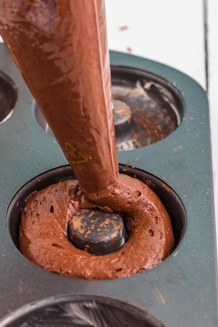 Close up of using a piping bag to pipe donut batter into pan