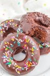 Close up of four chocolate donuts with chocolate icing and sprinkles on a white plate