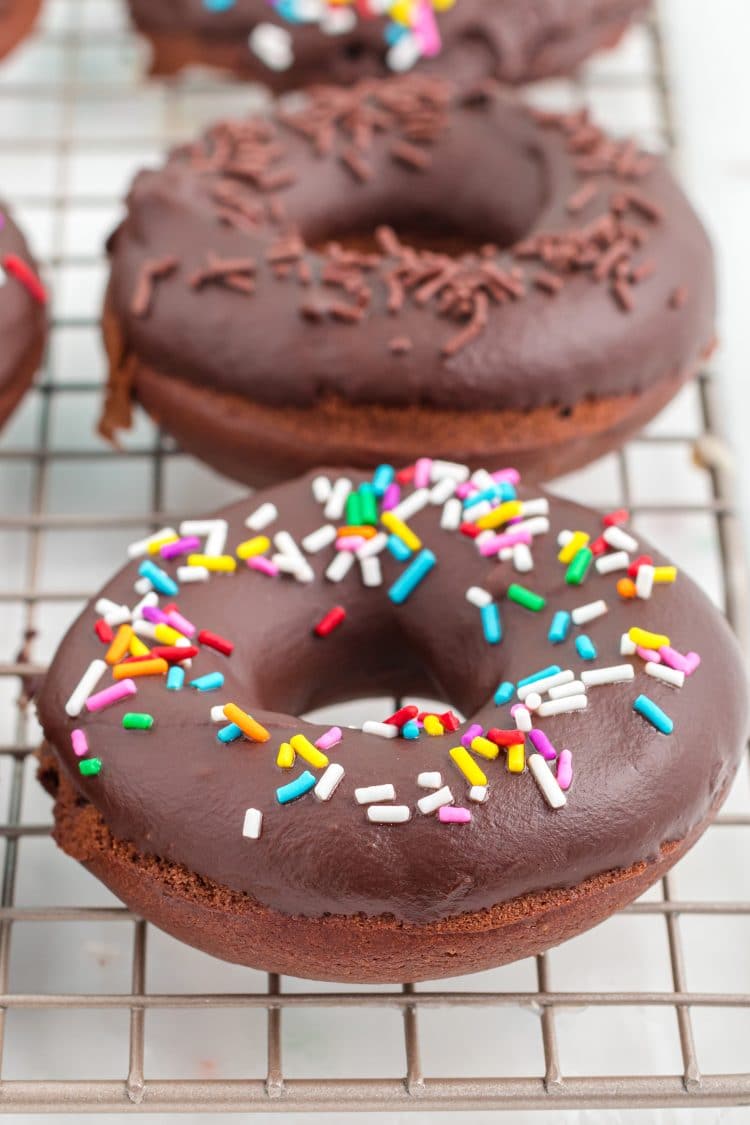 Chocolate donuts with rainbow sprinkles on wire rack