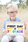 smiling schoolboy in glasses holding "first day of school" sign in the park