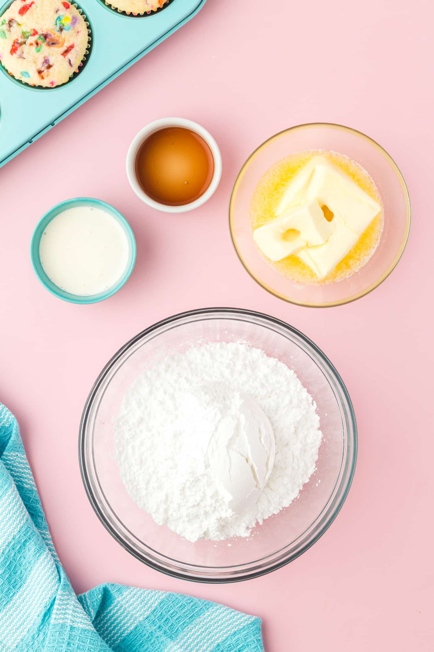 Vanilla buttercream frosting ingredients in individual bowls on pink background