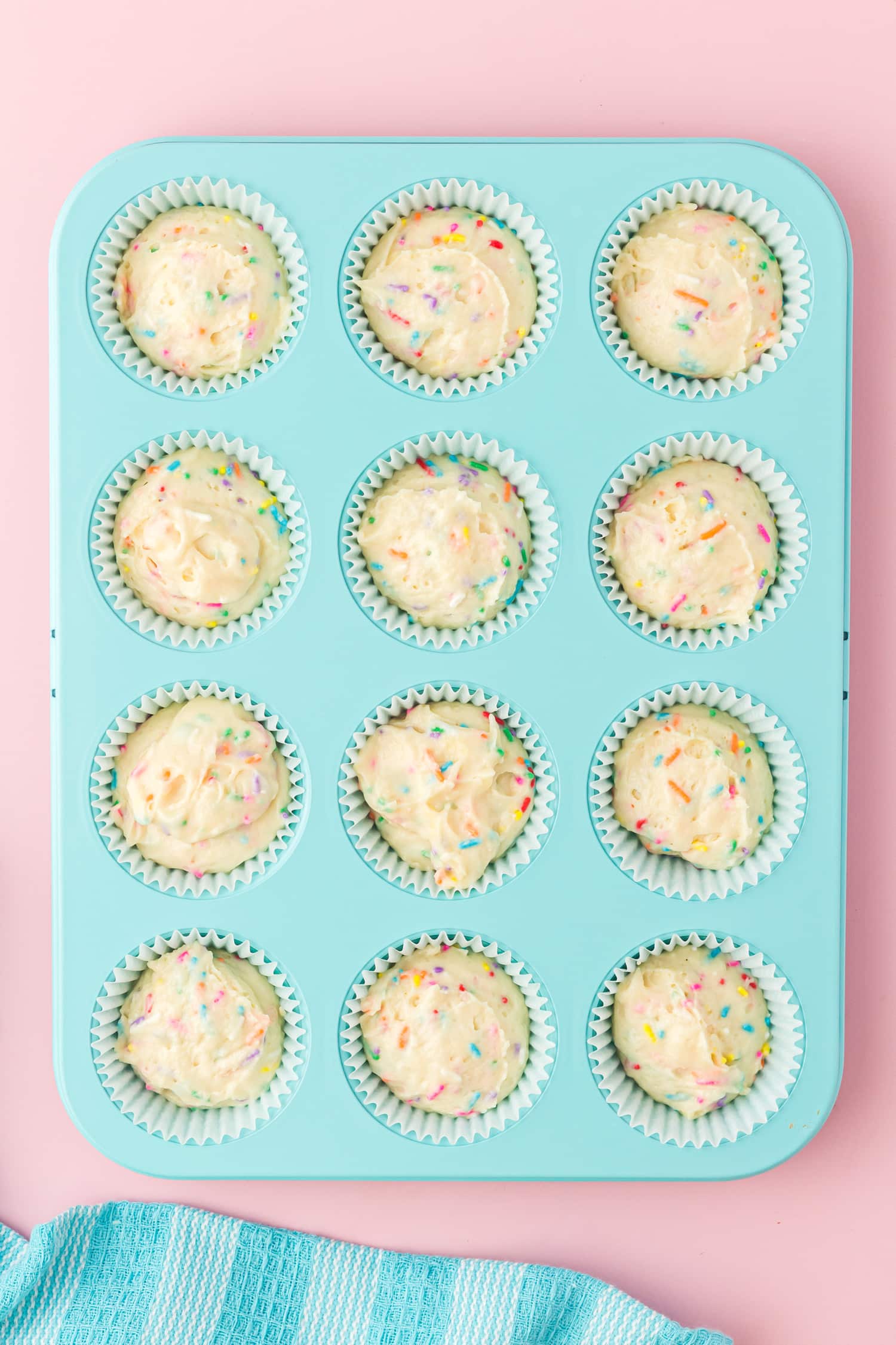 Funfetti cupcake batter in aqua colored muffin cupcake tin on pink backgound