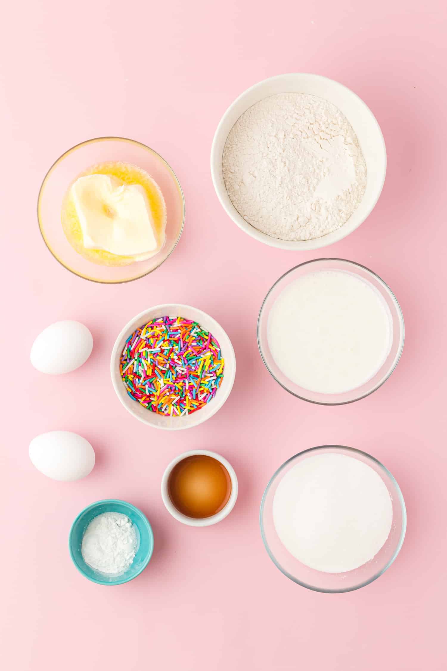 Bowls of individual Funfetti cupcake ingredients on pink background