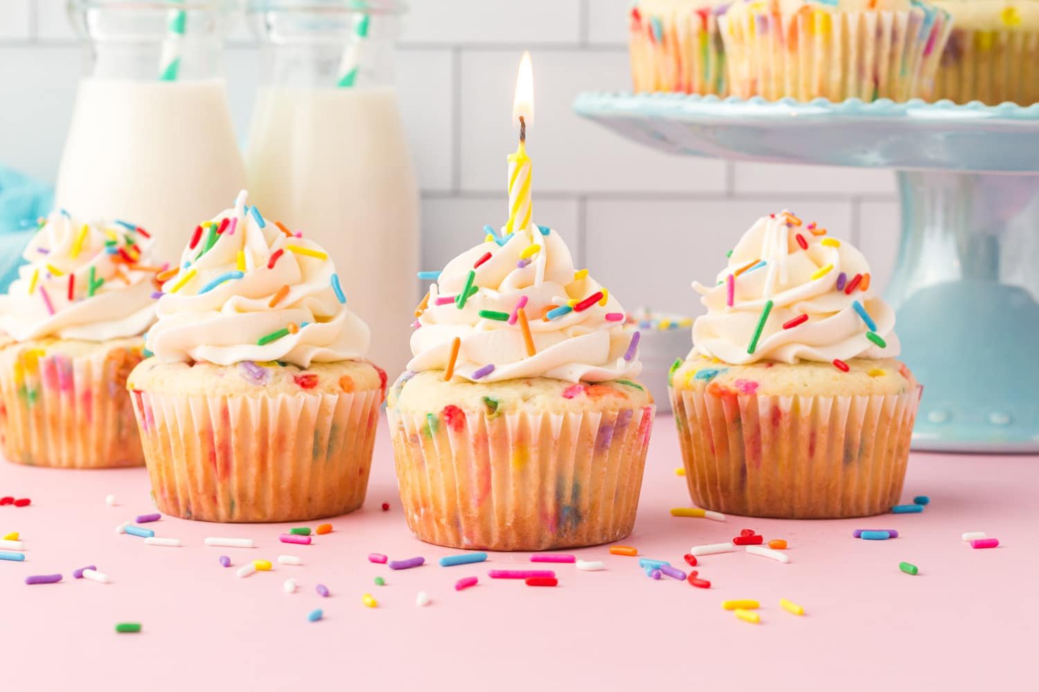 Funfetti cupcakes with one center birthday candle on pink background