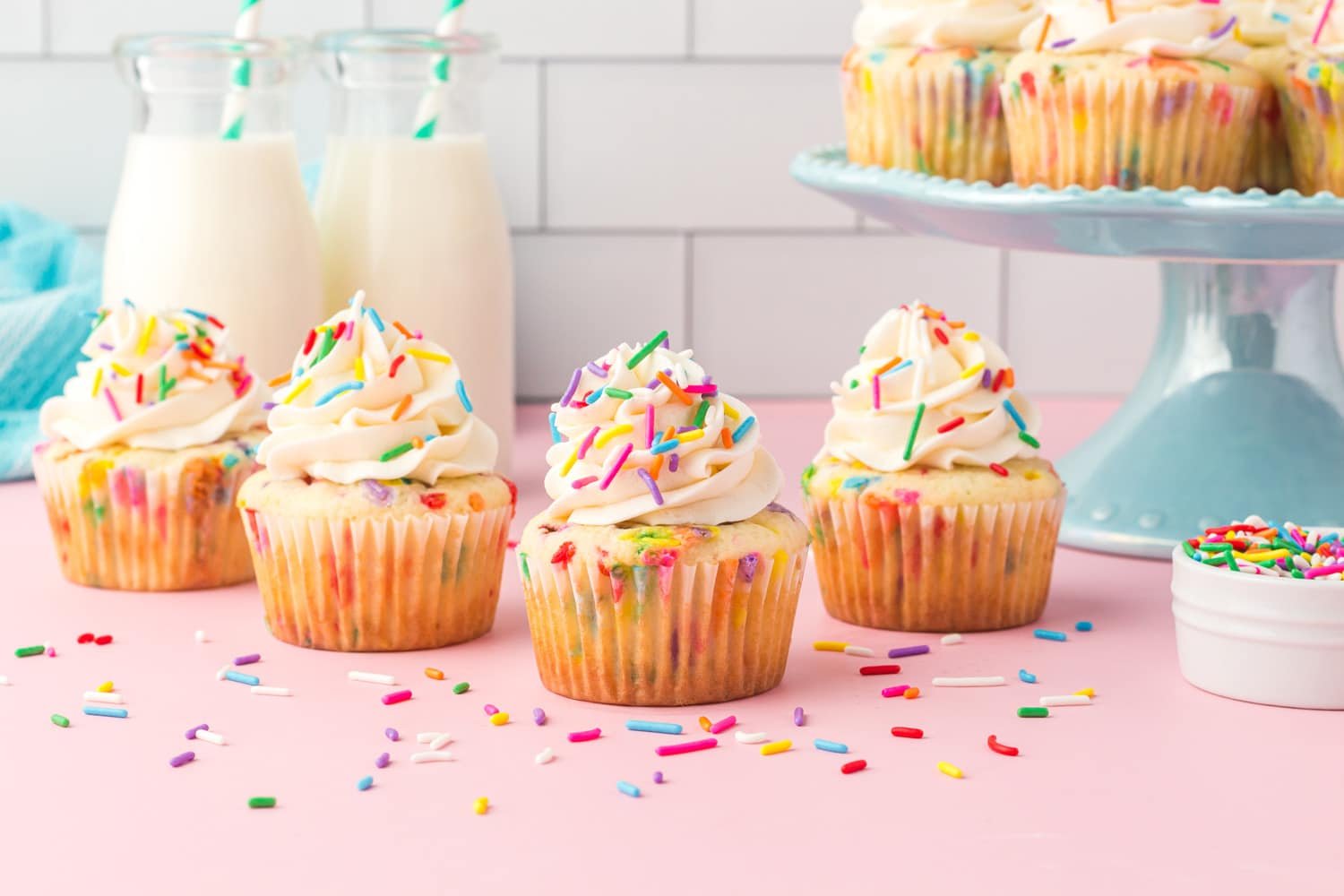 Four Funfetti cupcakes with vanilla buttercream icing on a pink background with sprinkles