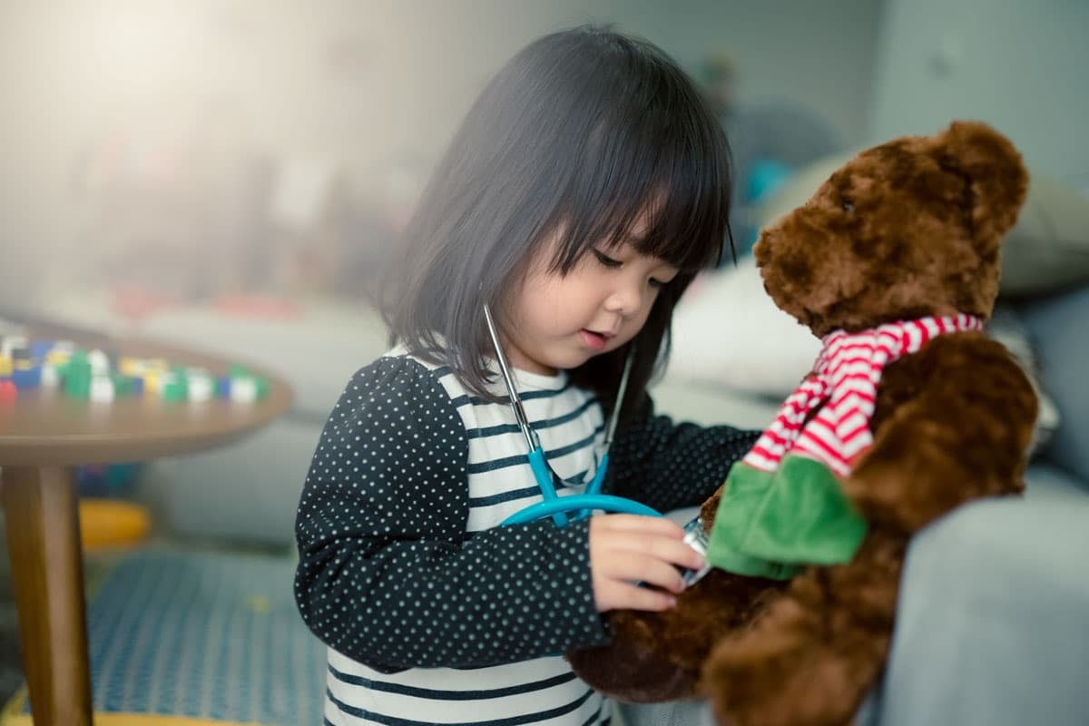 Little Asian girl holding a stethoscope in hand and checking teddy bear.