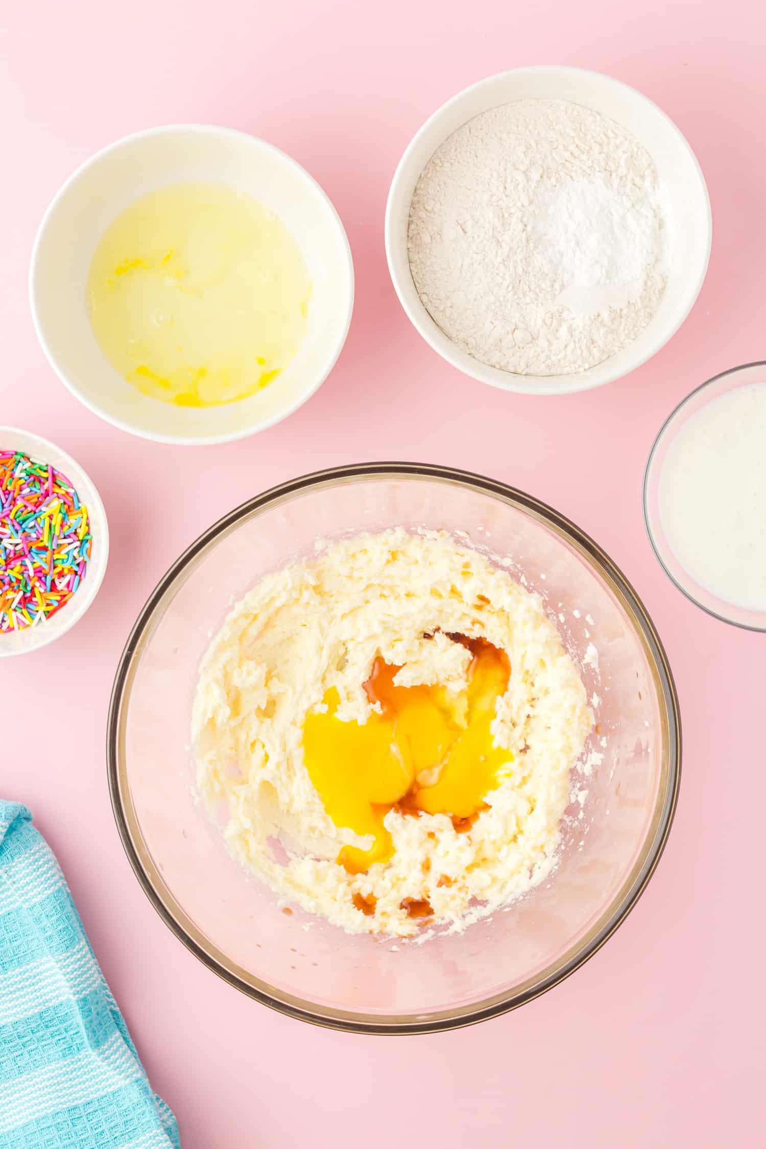 egg yolks and other wet Funfetti cupcakes ingredients in glass bowl on pink background
