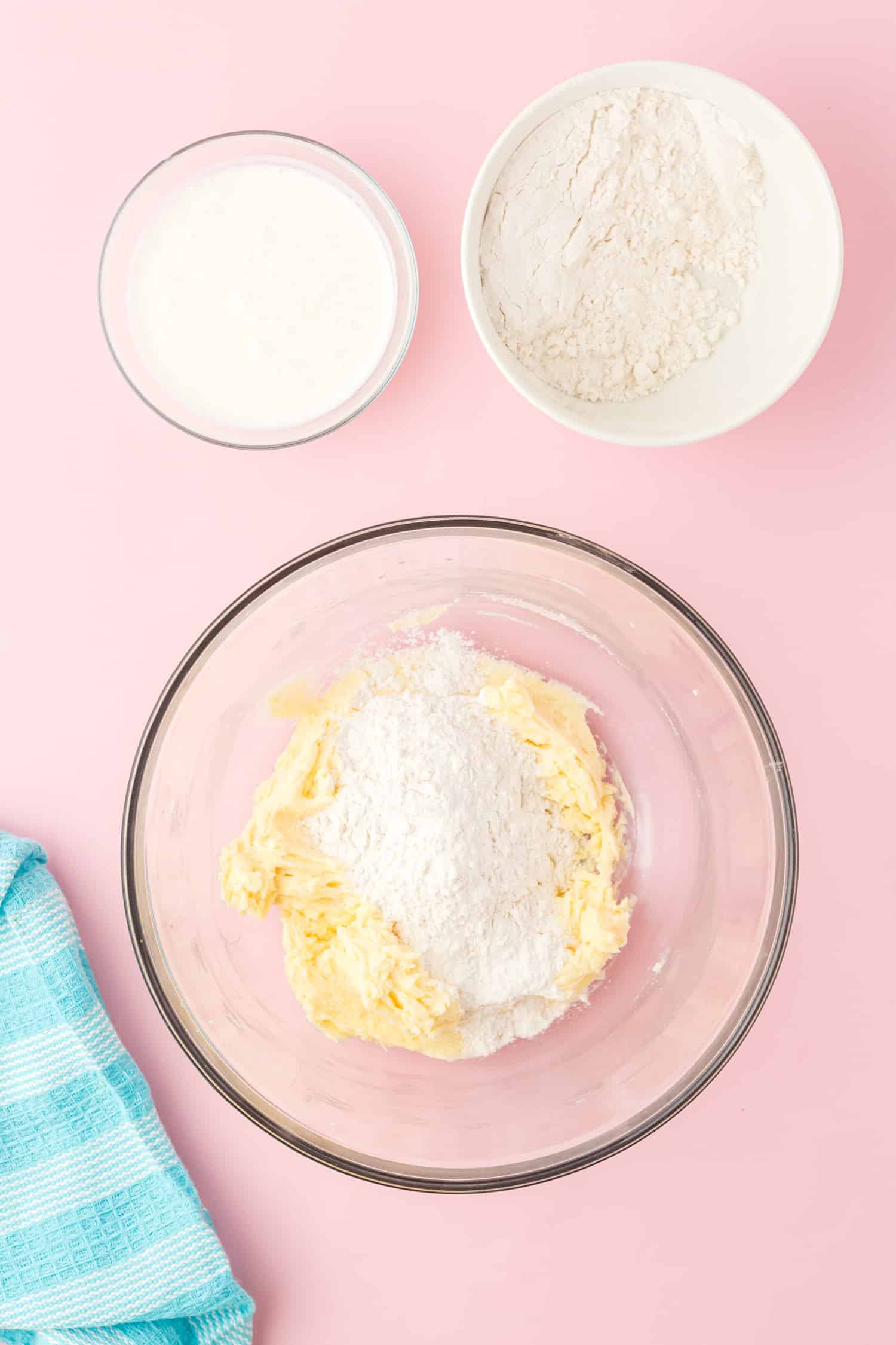 adding dry Funfetti cupcake ingredients to the wet mixture in glass bowl on a pink background