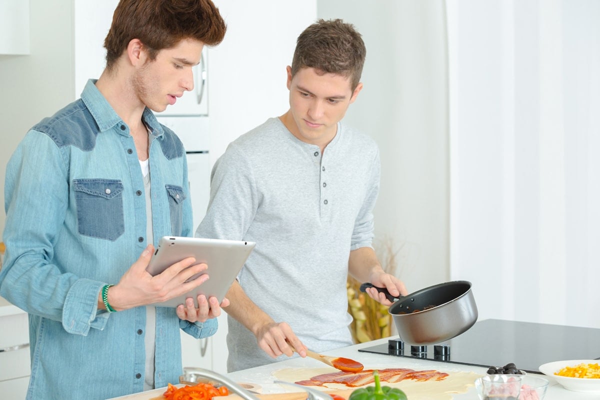 Two high school young men cooking pizza dinner in kitchen at home