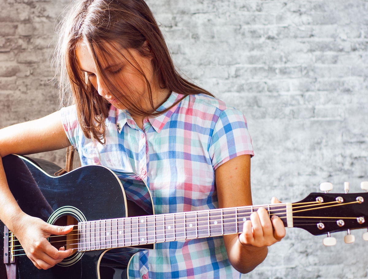 Teen girl with long hair playing acoustic guitar
