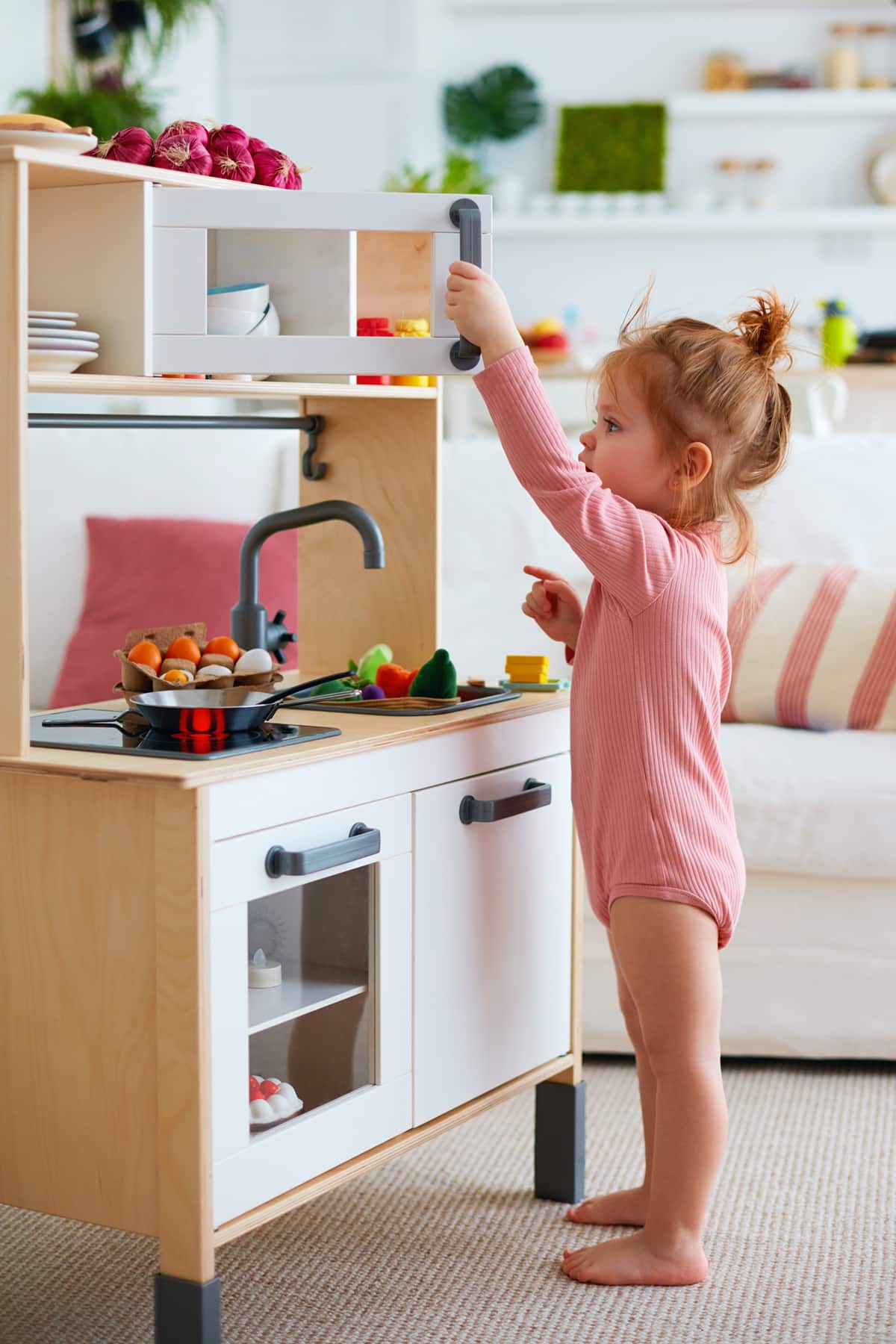 cute red-haired toddler girl playing on toy kitchen at home
