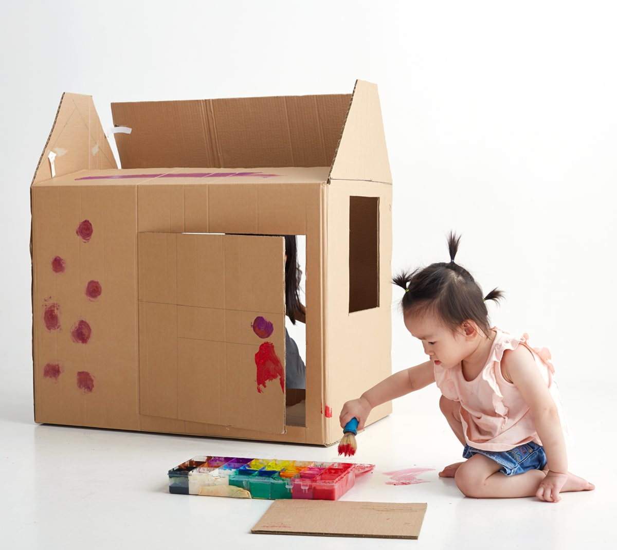 Asian toddler painting a large cardboard box playhouse