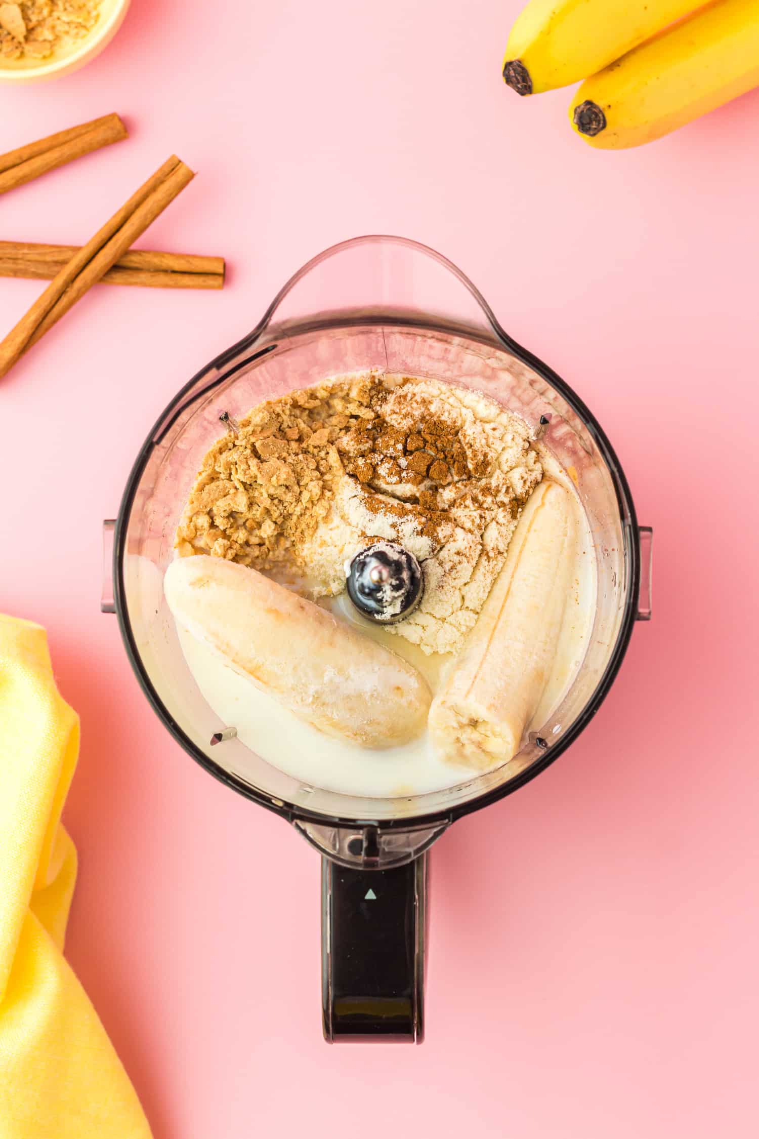 Overhead shot of banana cream pie ingredients in blender on pink background