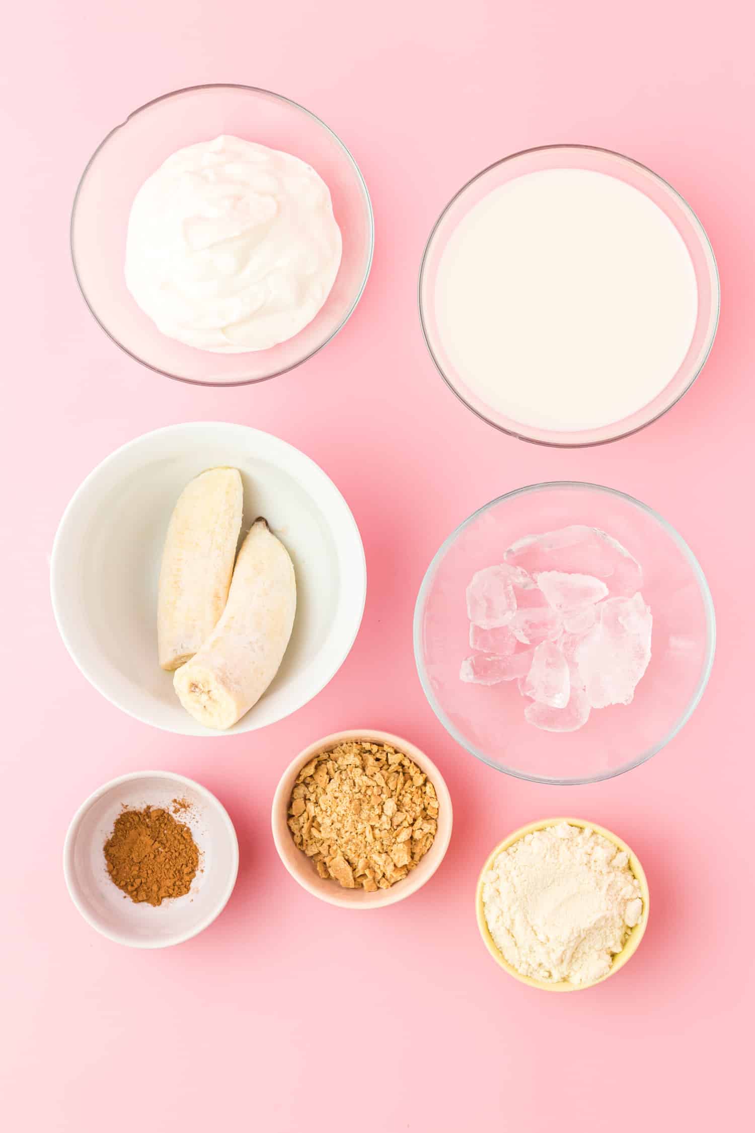 Ingredients for banana cream pie smoothie in individual bowls on pink background