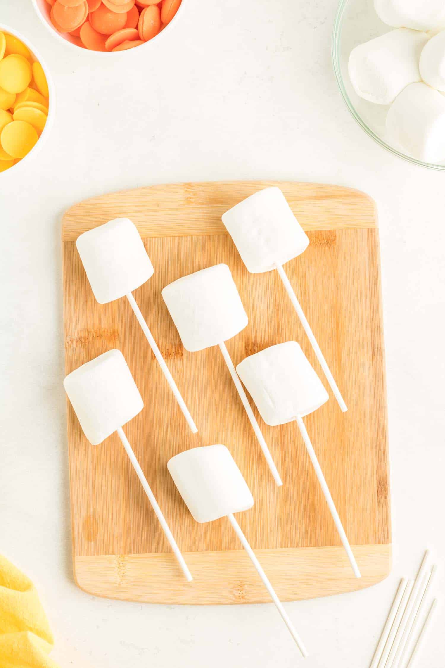 Six marshmallow pops on wooden cutting board.