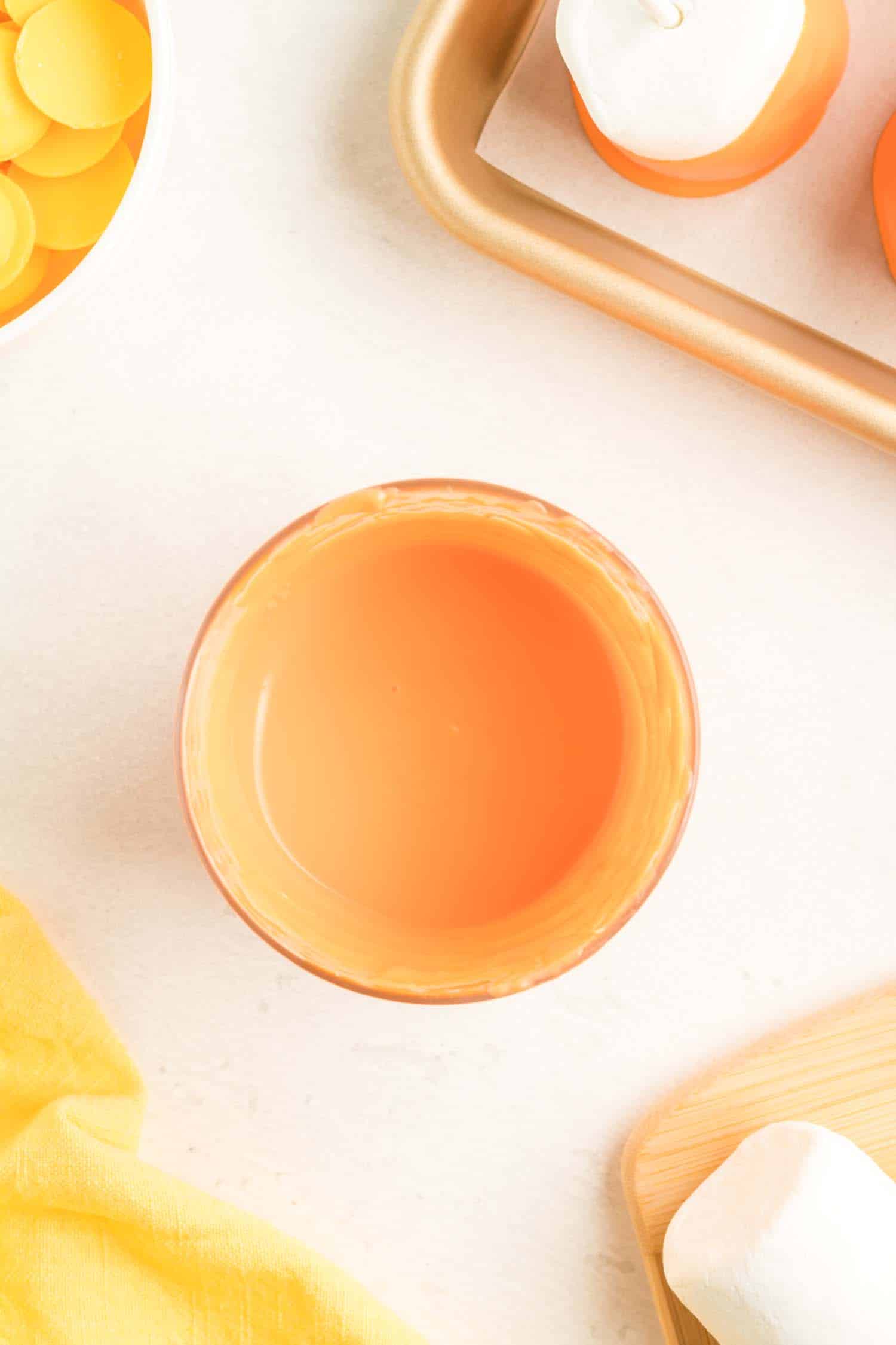 Melted orange candy melts in a glass bowl on a white table.