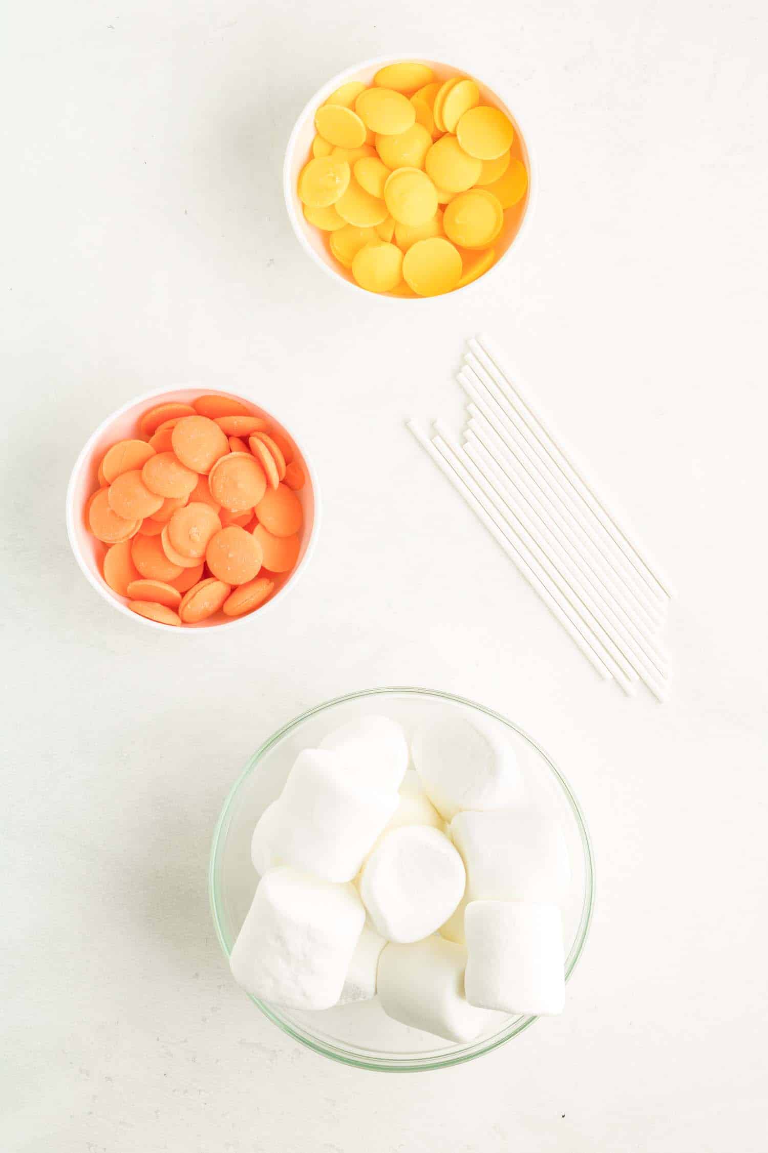 Ingredients in a glass bowl to make candy corn marshmallow pops.