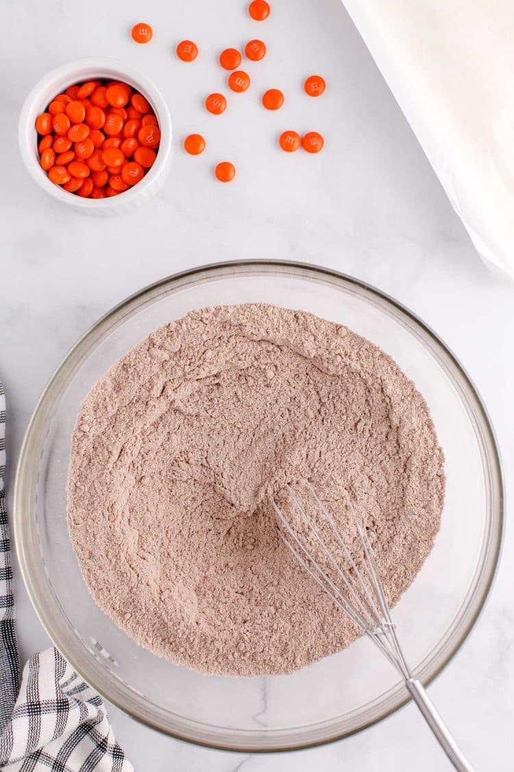 Whisking chocolate cake mix in a glass bowl on a white table.